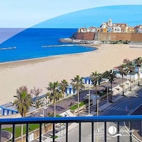 A coastal hotel with a beach view, palm trees, and a clear blue sky.