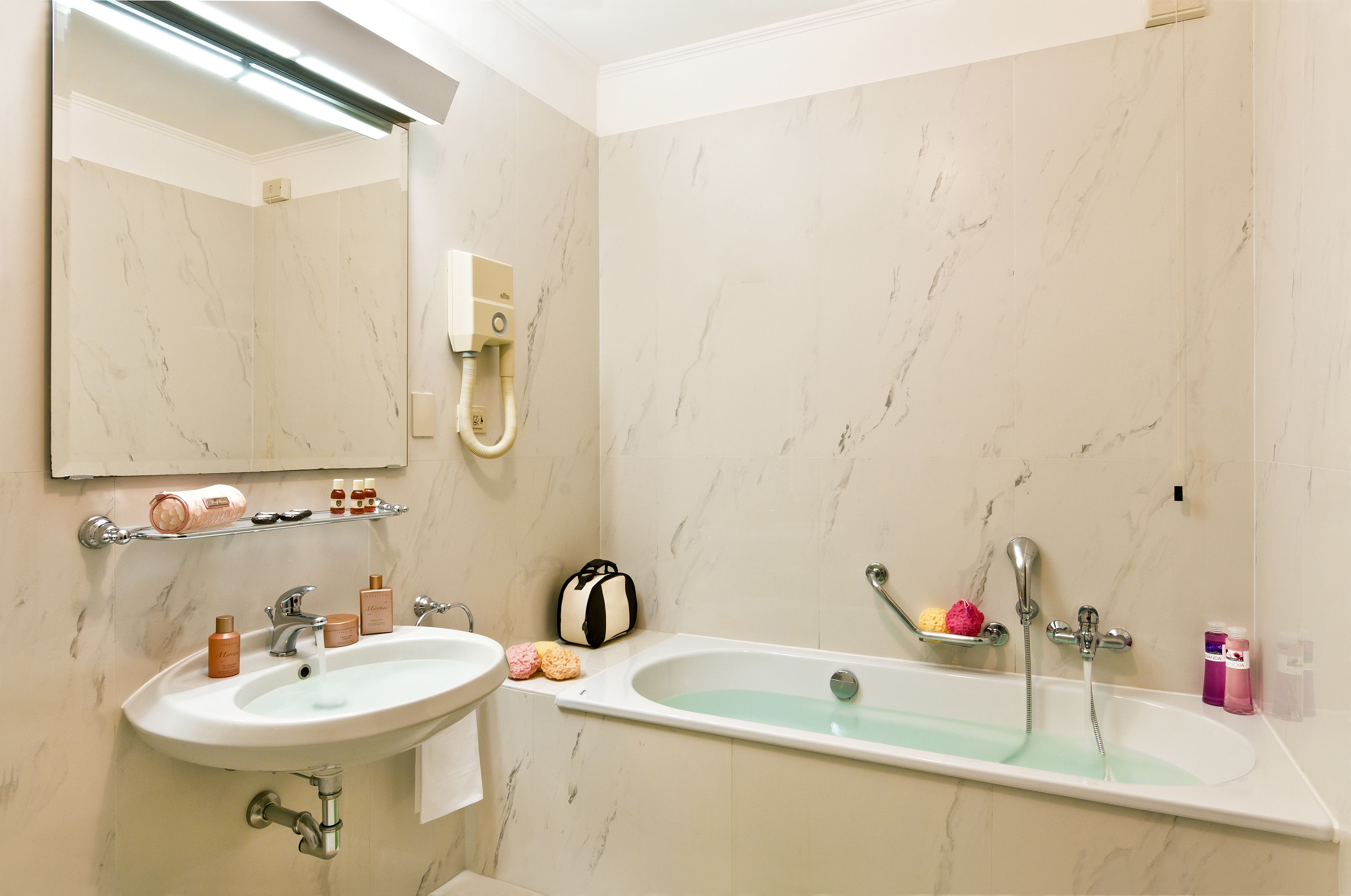 A bathroom with a sink, mirror, and bathtub. There are toiletries on the sink and a towel rack.