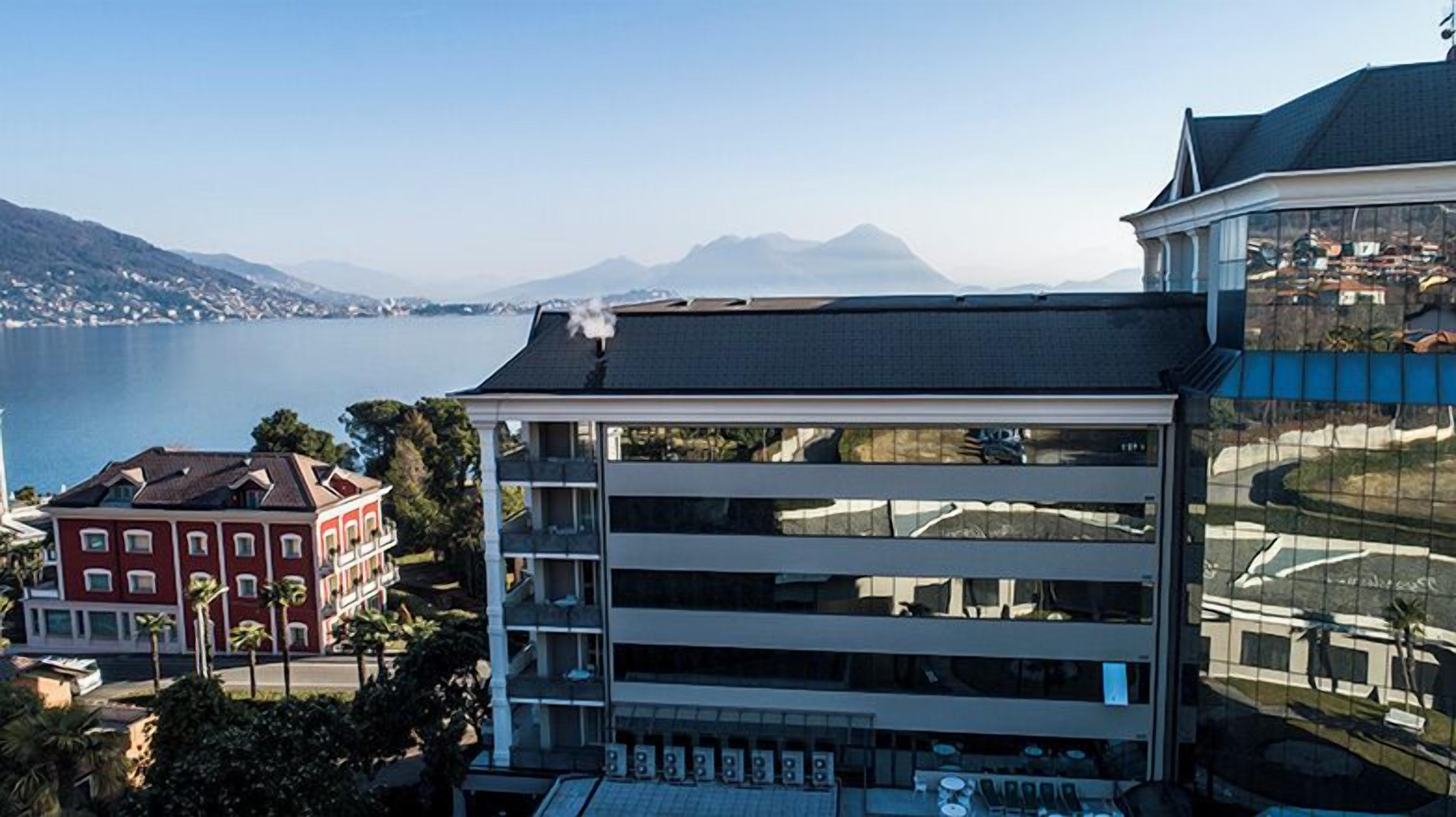 A modern building with multiple floors, large windows, and a view of a lake and mountains in the background.