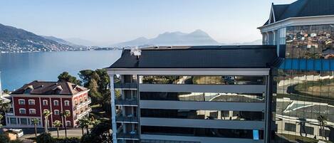 A modern building with multiple floors, large windows, and a view of a lake and mountains in the background.
