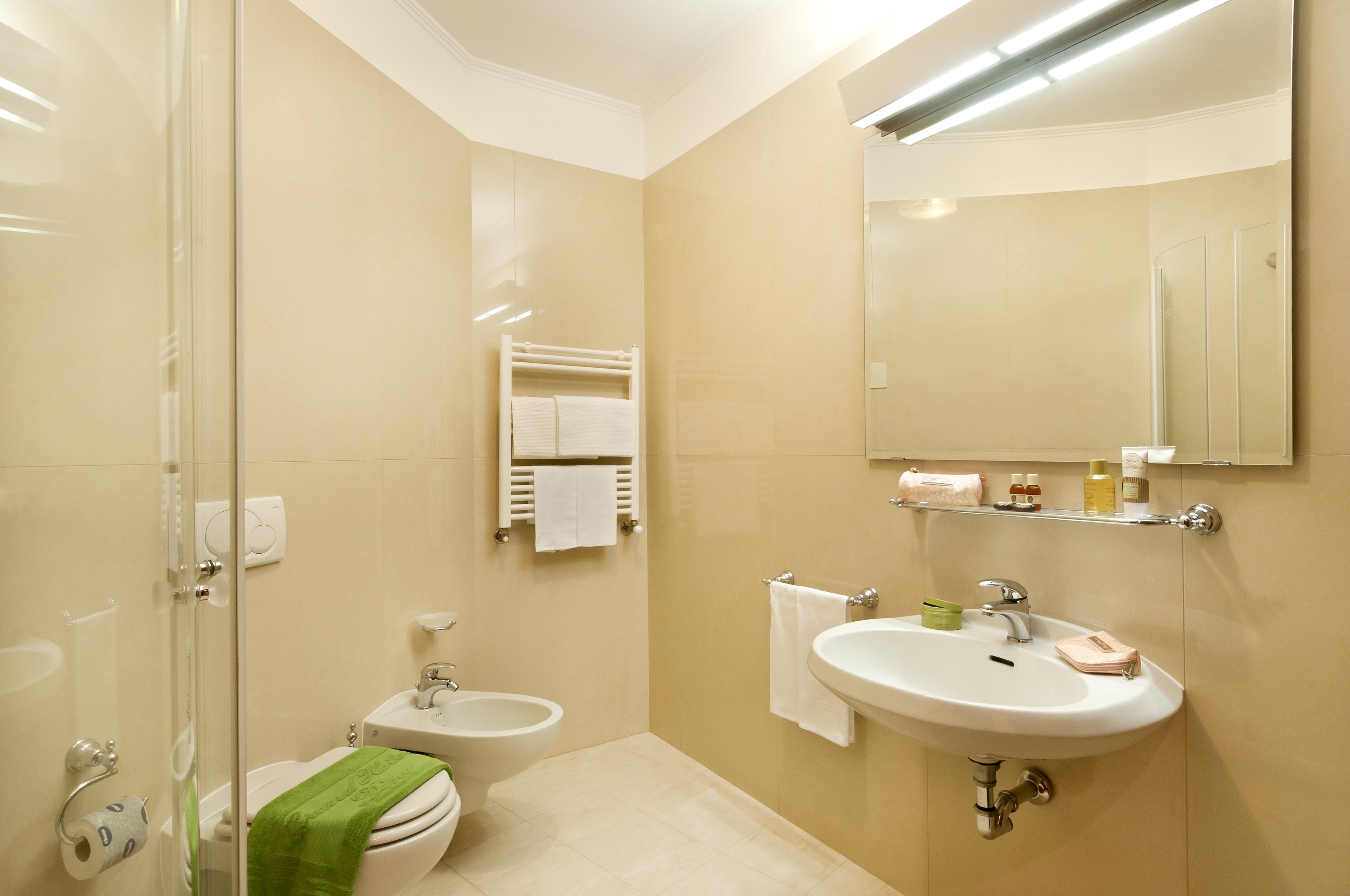 Une salle de bain moderne avec une douche à parois de verre, des toilettes, un bidet, un lavabo avec un miroir et un porte-serviettes.