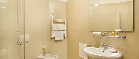 Une salle de bain moderne avec une douche à parois de verre, des toilettes, un bidet, un lavabo avec un miroir et un porte-serviettes.