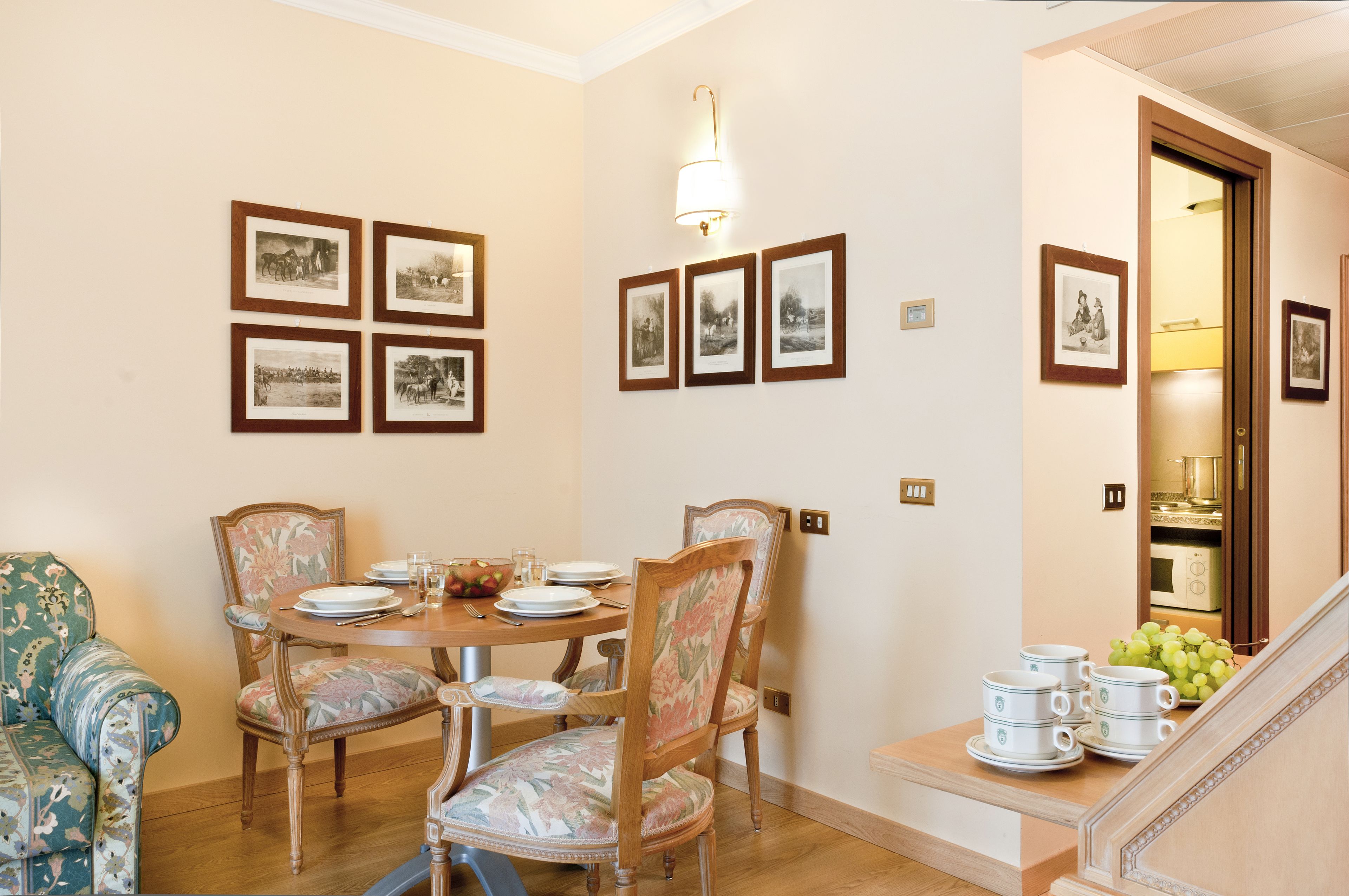 A dining area with a round table, floral chairs, and framed pictures on the wall.