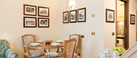 A dining area with a round table, floral chairs, and framed pictures on the wall.