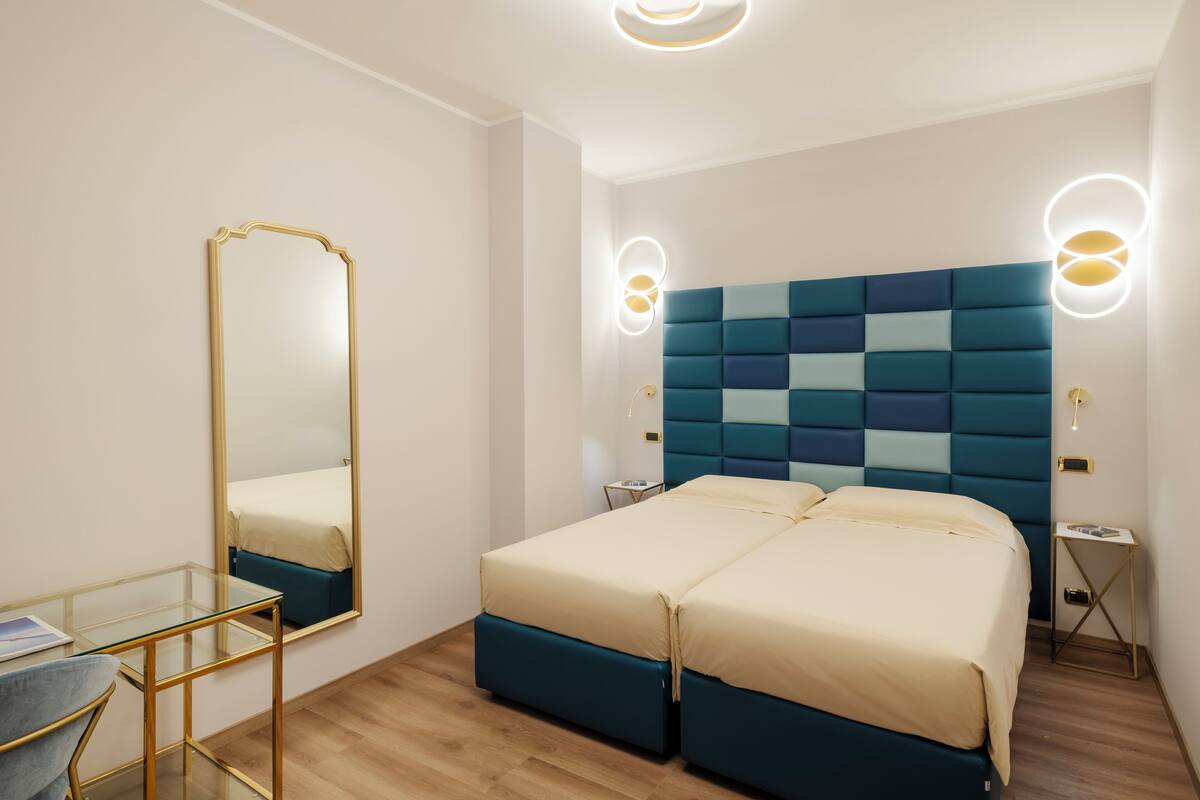Una habitación de hotel moderna con dos camas, un escritorio de vidrio y un espejo grande.
