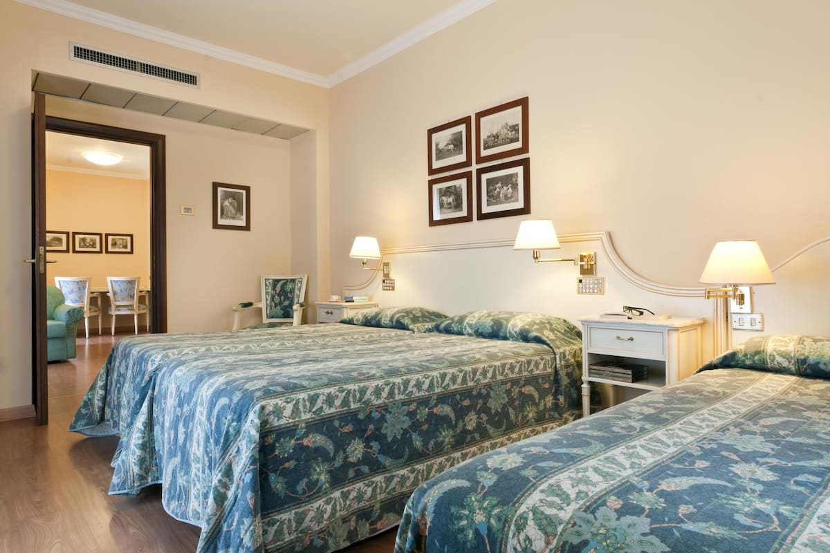 Habitación de hotel con dos camas, una mesita de noche, una silla y un escritorio. Hay lámparas de pared y cuadros en la pared.