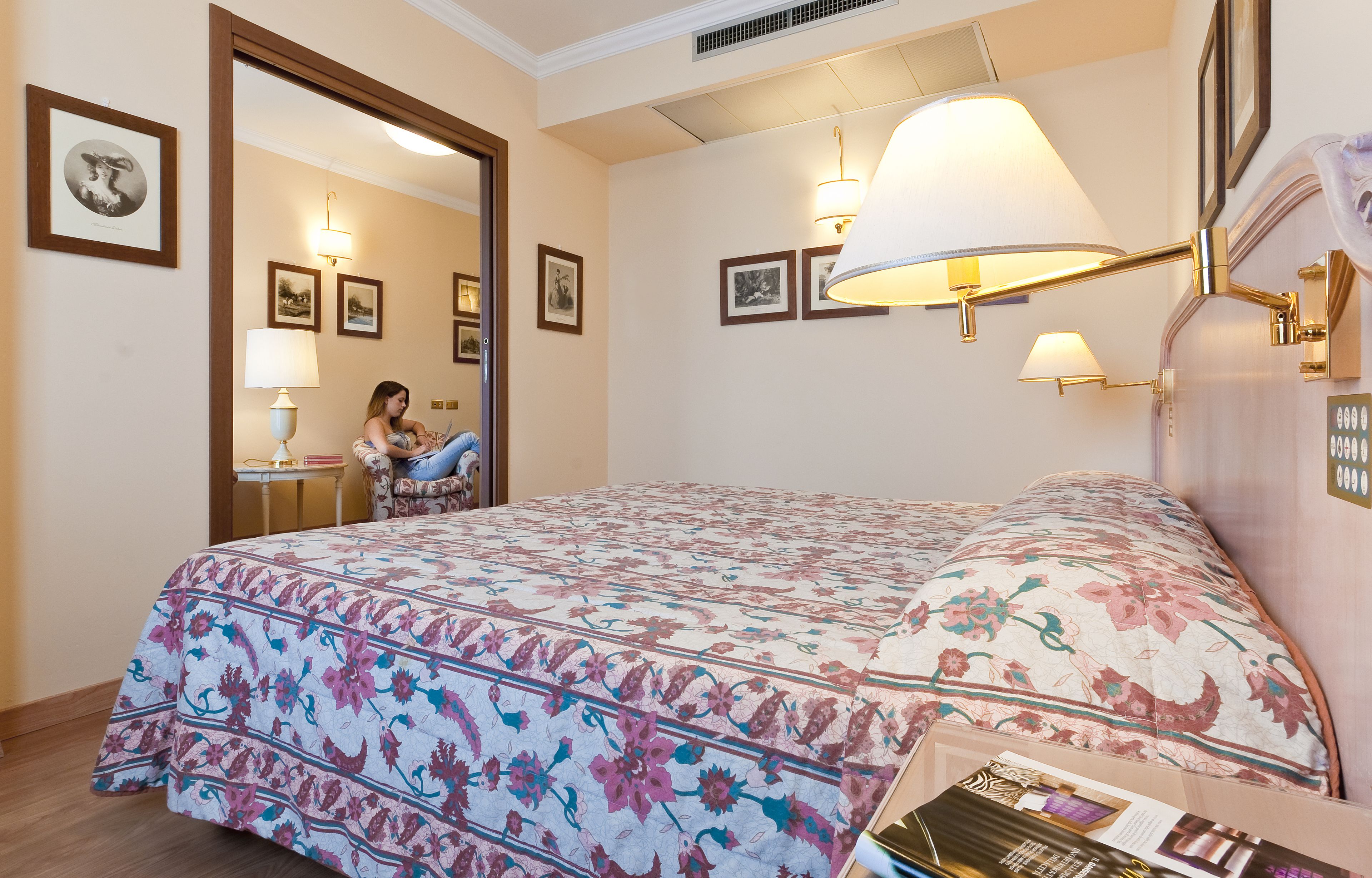 Quarto de hotel com uma cama grande, um espaço de estar com uma poltrona e uma mesa, e um espelho.