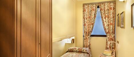 A bedroom with a bed, a chair, a wardrobe, and a window with curtains.