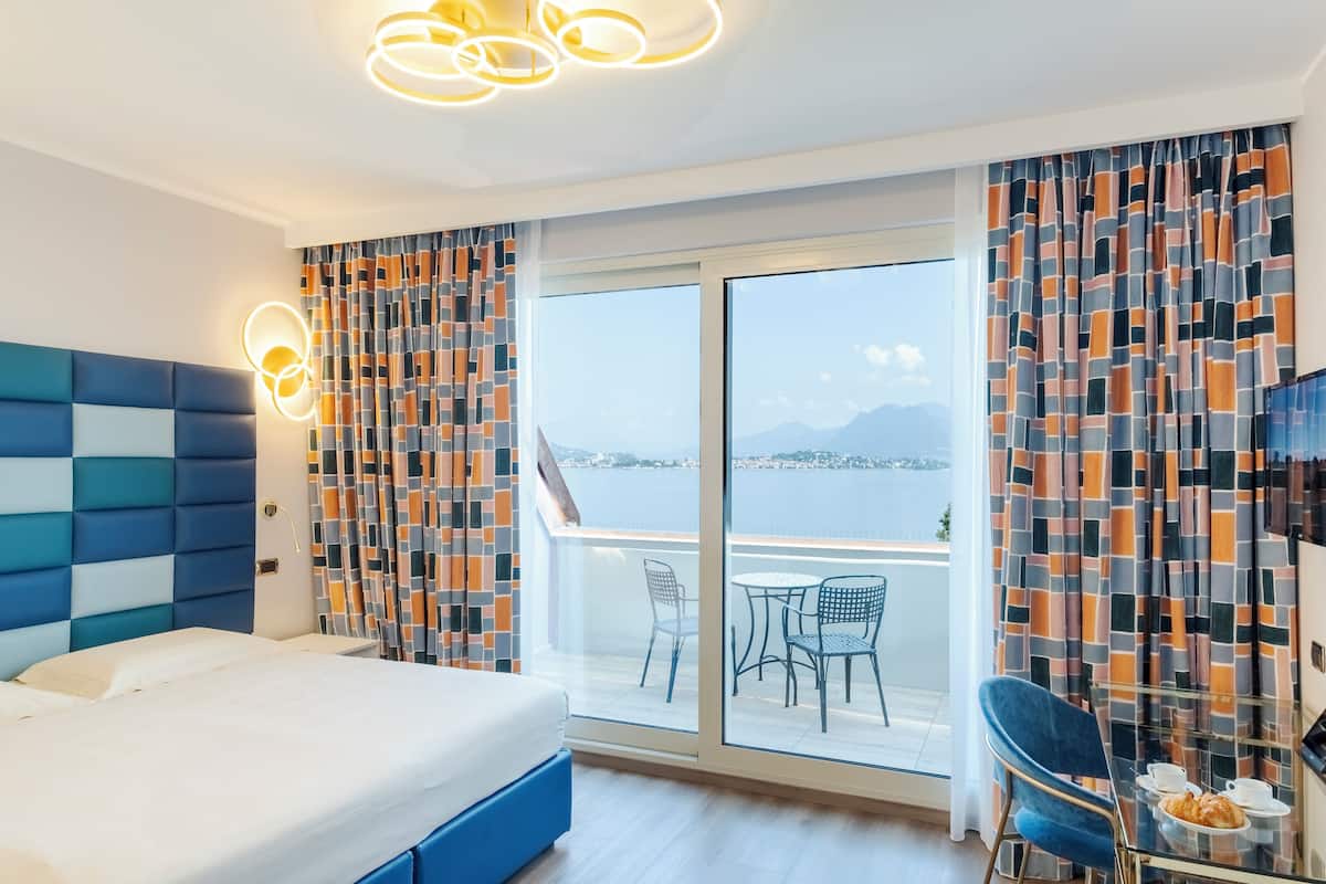 Una habitación de hotel moderna con una cama grande, un balcón con mesa y sillas, y vistas al mar.