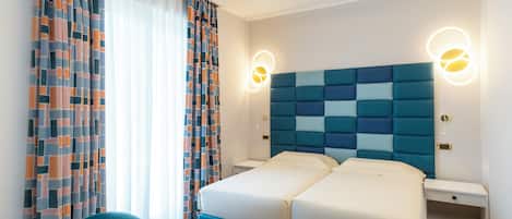 A hotel room with a double bed, two bedside tables, a chair, and a large window with curtains.