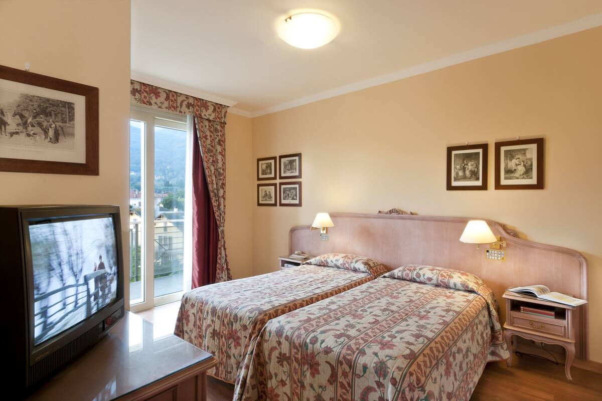 Una habitación de hotel con cama, televisor, mesita de noche y ventana con cortinas.