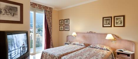 A hotel room with a bed, a television, a nightstand, and a window with curtains.
