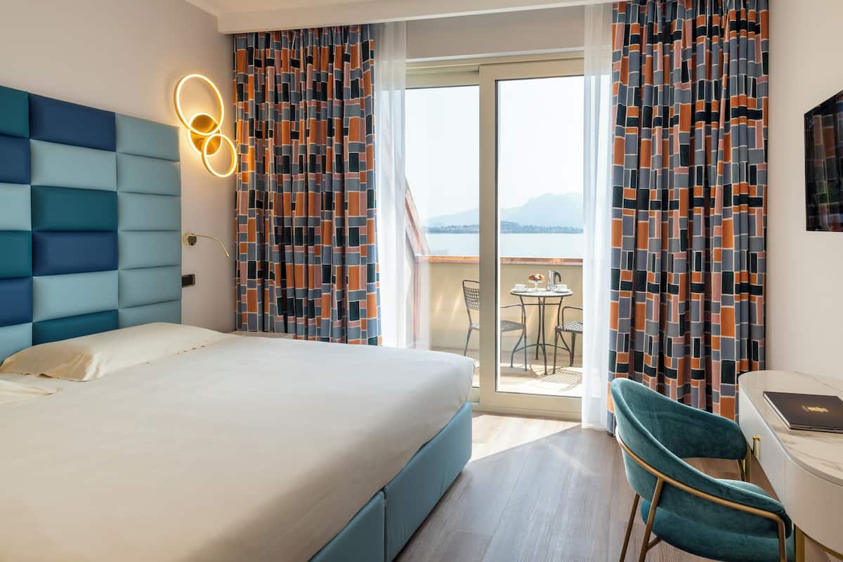 Habitación de hotel con una cama grande, un escritorio con una computadora portátil, una silla y un balcón con vistas al agua.