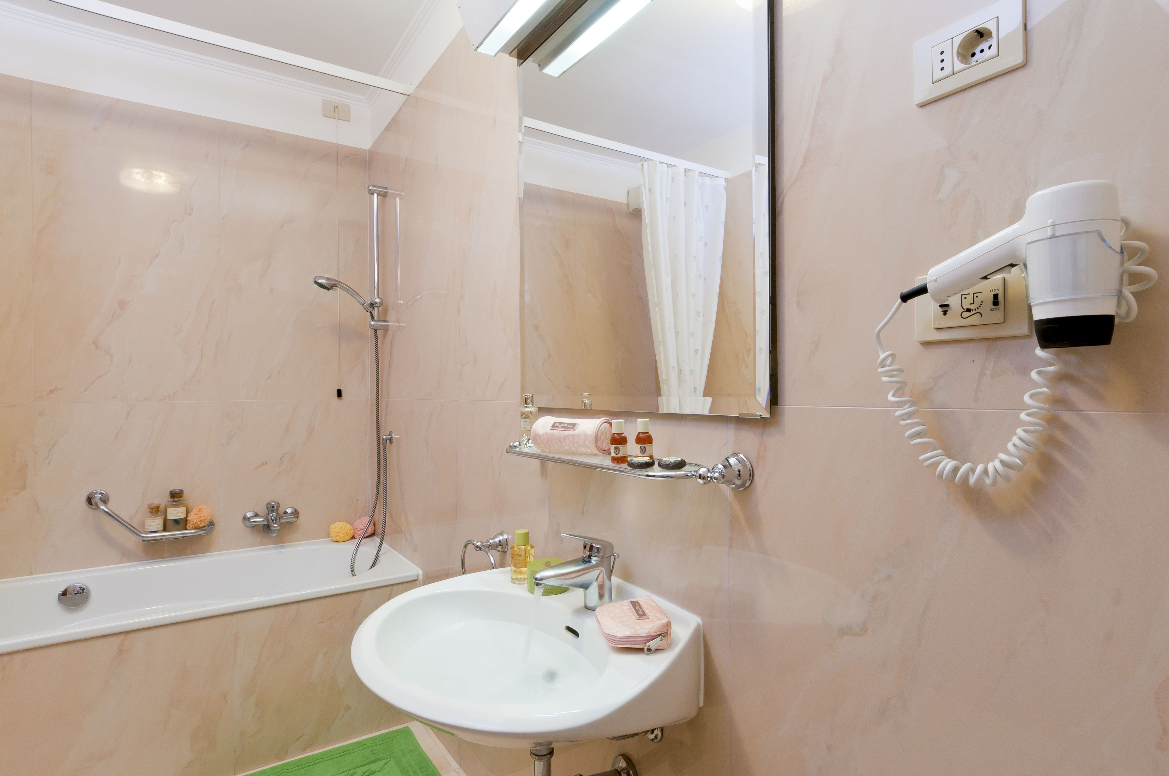 A bathroom with a bathtub, a sink, a hairdryer mounted on the wall, and a mirror above the sink.