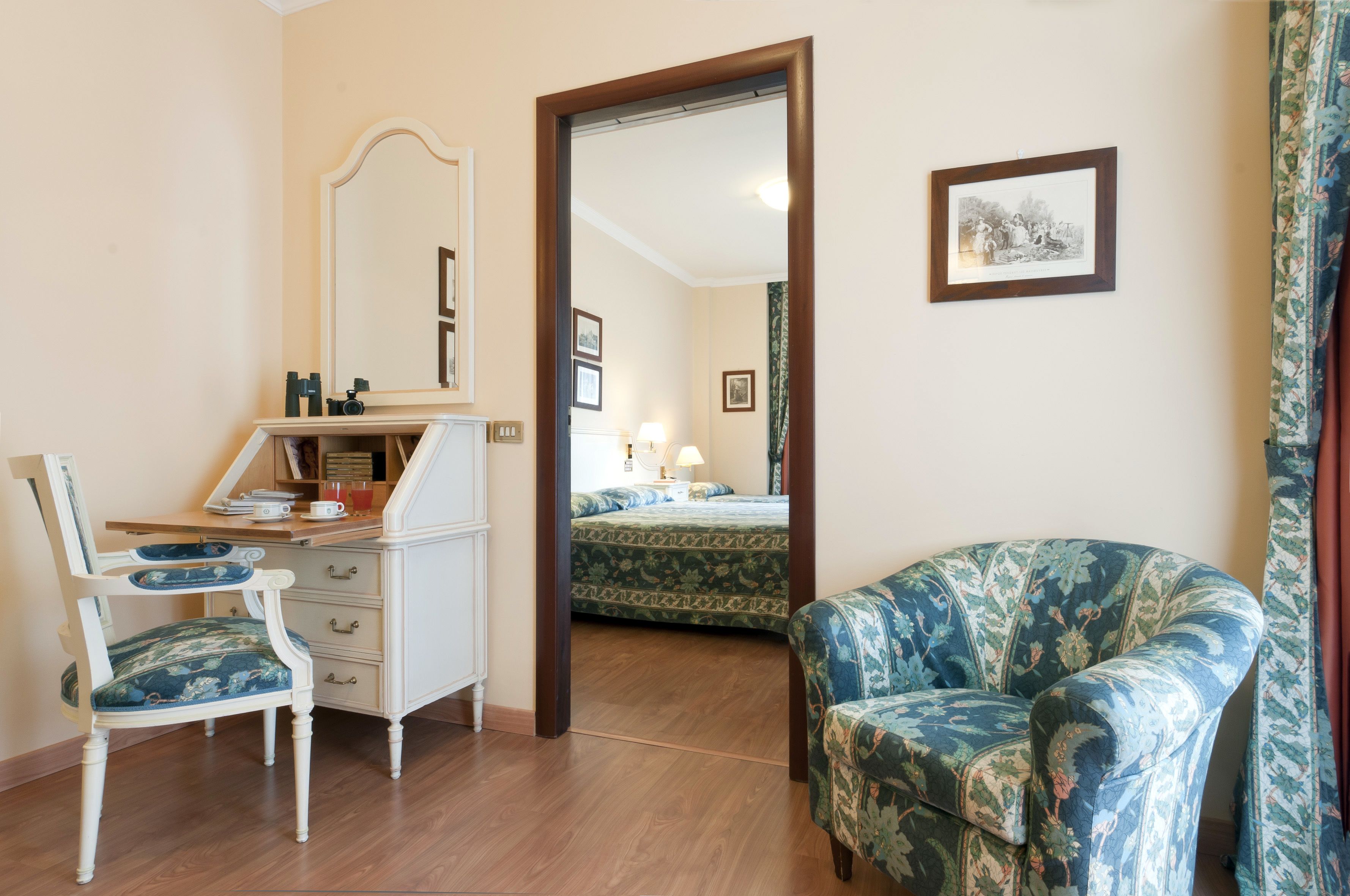 A room with a wooden desk, a chair, a bed with a patterned bedspread, and a framed picture on the wall.