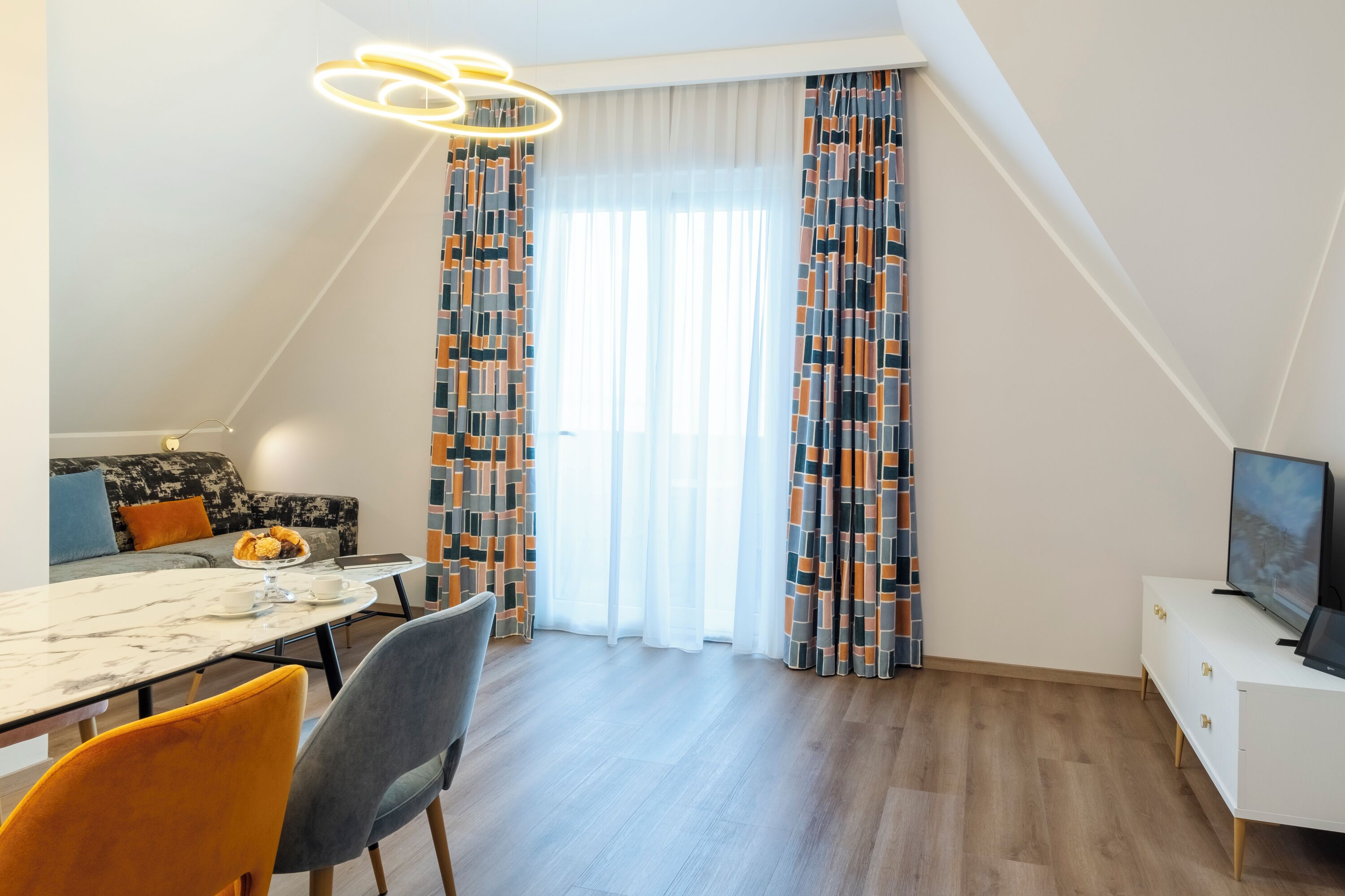 Una sala de estar moderna con comedor, que incluye un sofá, un televisor, una mesa de comedor con sillas y un ventanal con cortinas estampadas.