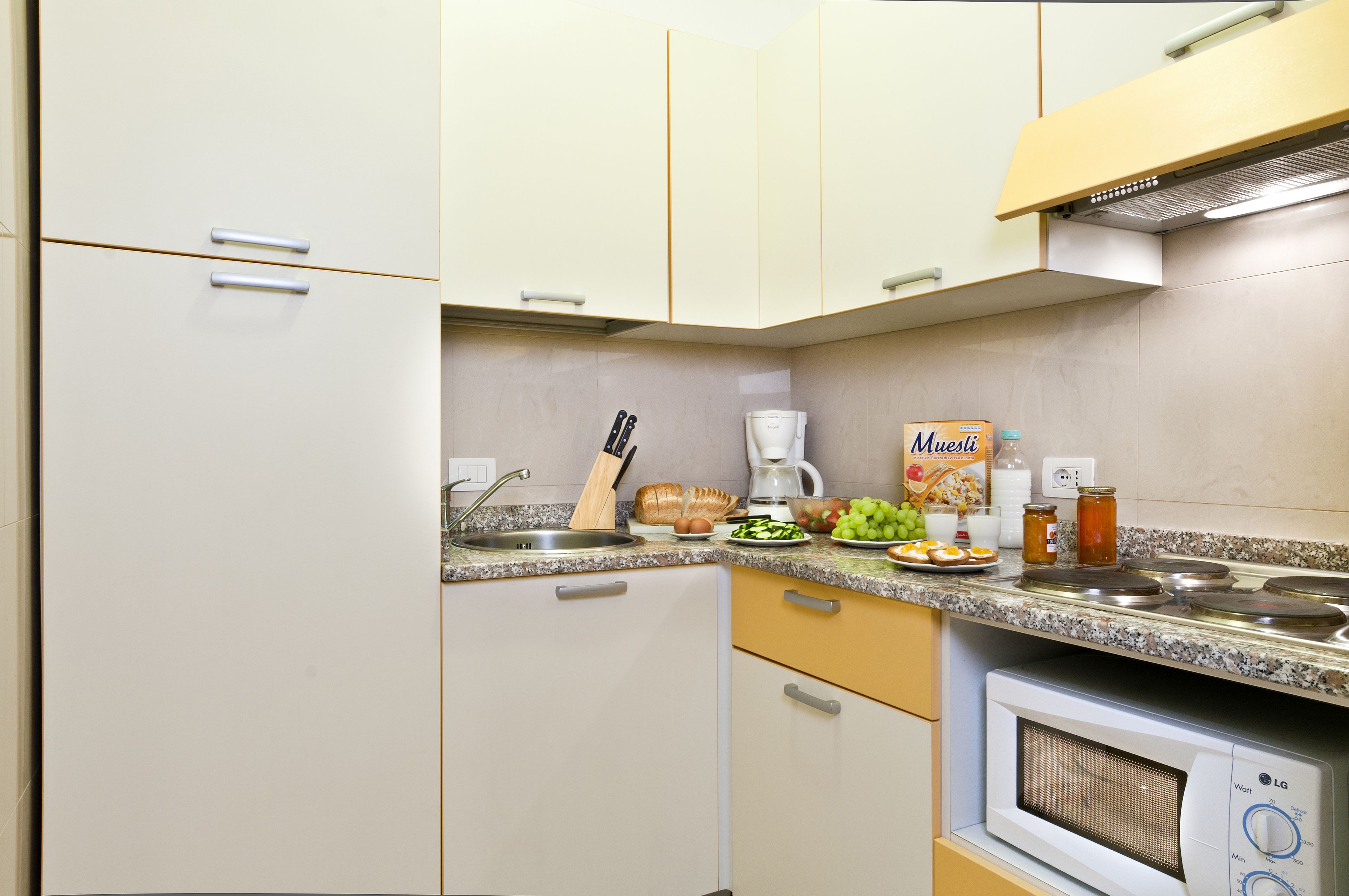 A compact kitchen with a microwave, a coffee maker, and a variety of food items on the counter.