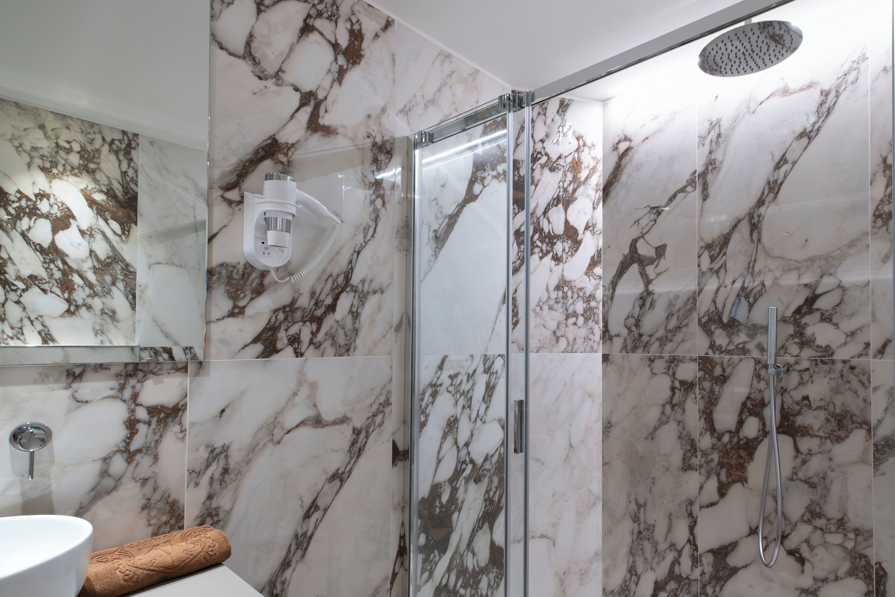Un baño con ducha cubierta por vidrio, un revestimiento de mármol y un lavamanos blanco.