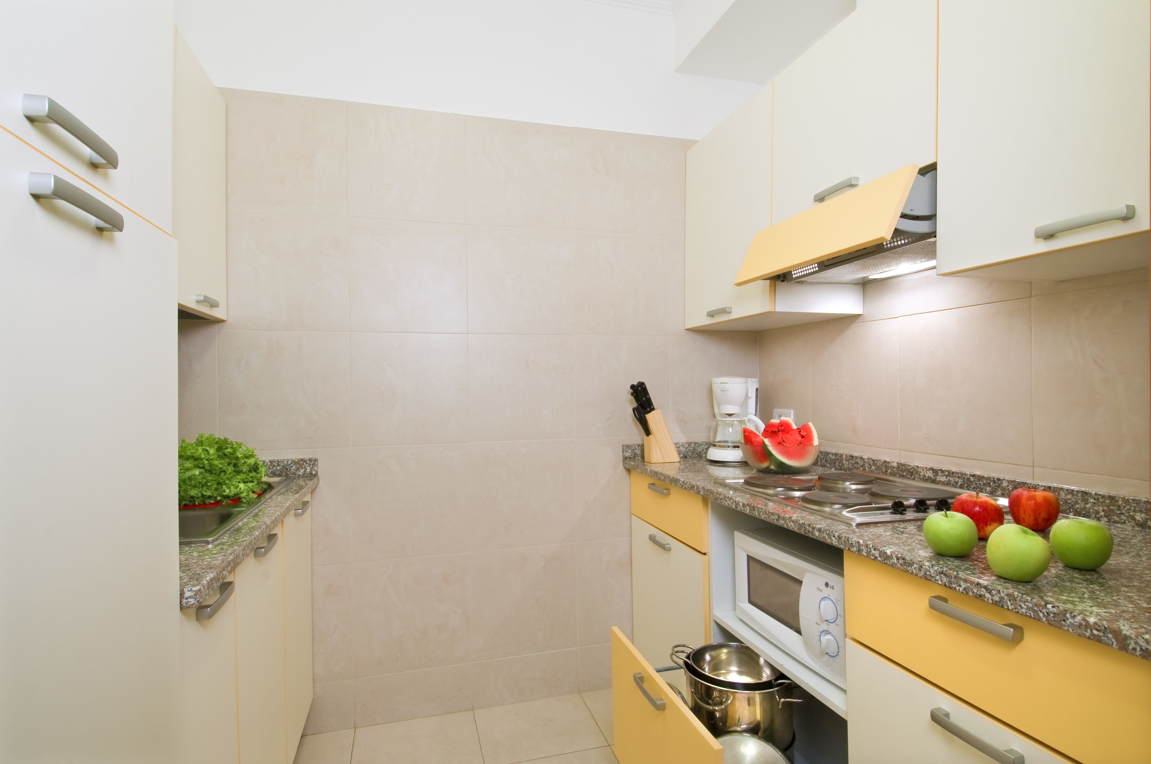 A compact kitchen with a microwave, stove, and countertop with fruits and a knife.