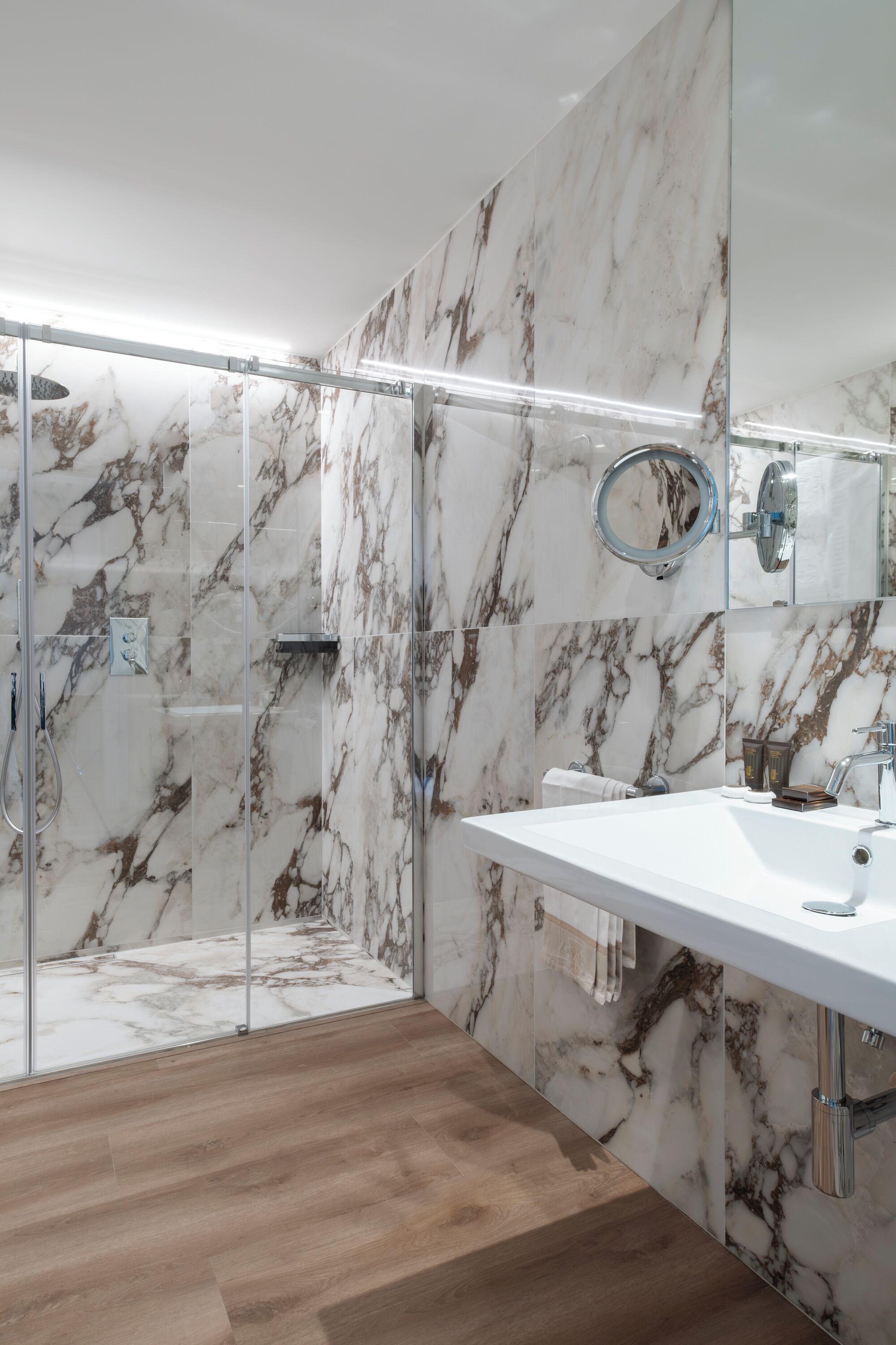 Ein modernes Badezimmer mit Marmorwand, einer Duschkabine aus Glas und einem weißen Waschbecken.