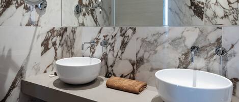 Baño con dos lavamanos tipo recipiente, una toalla y un espejo.