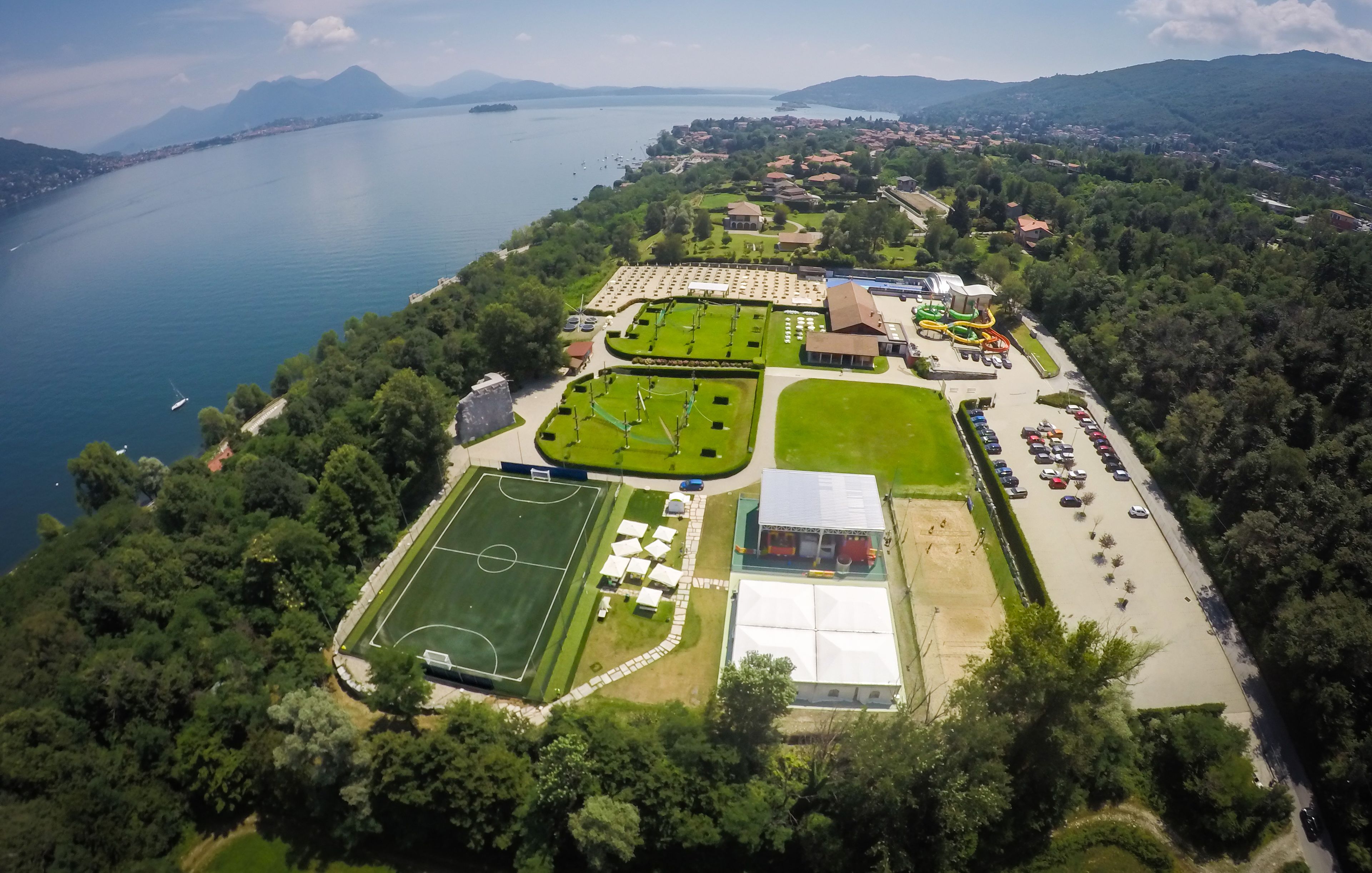 Vista aérea de un complejo turístico con varias canchas deportivas, un estacionamiento y un lago.