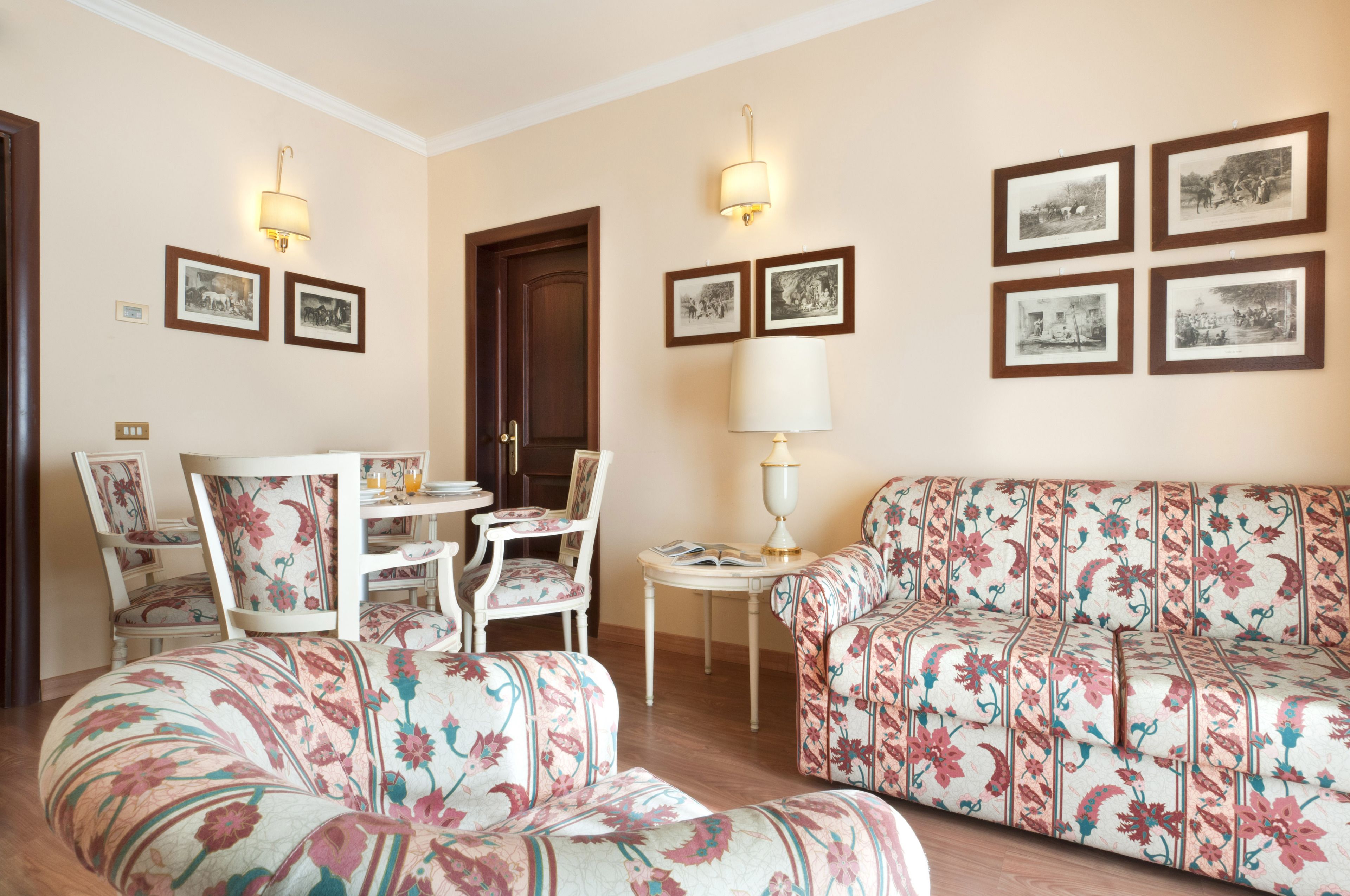 Un salon avec des canapés et des fauteuils à motifs floraux, une table à manger avec des chaises, et des tableaux encadrés accrochés aux murs.