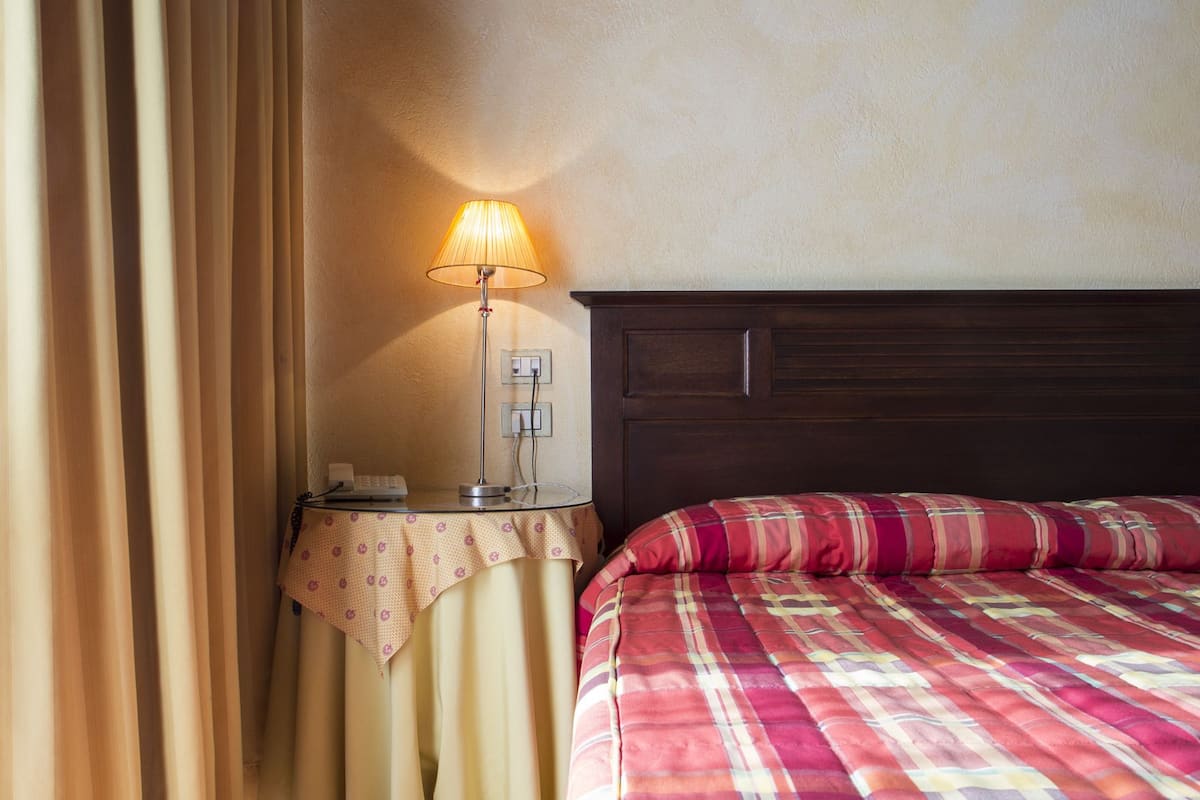 A hotel room with a bed, a bedside table with a lamp, and a curtain.