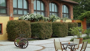 A building with a brick facade, large arched windows, and a garden area with a table and chairs. - Tenuta La Cascinetta (Buriasco)