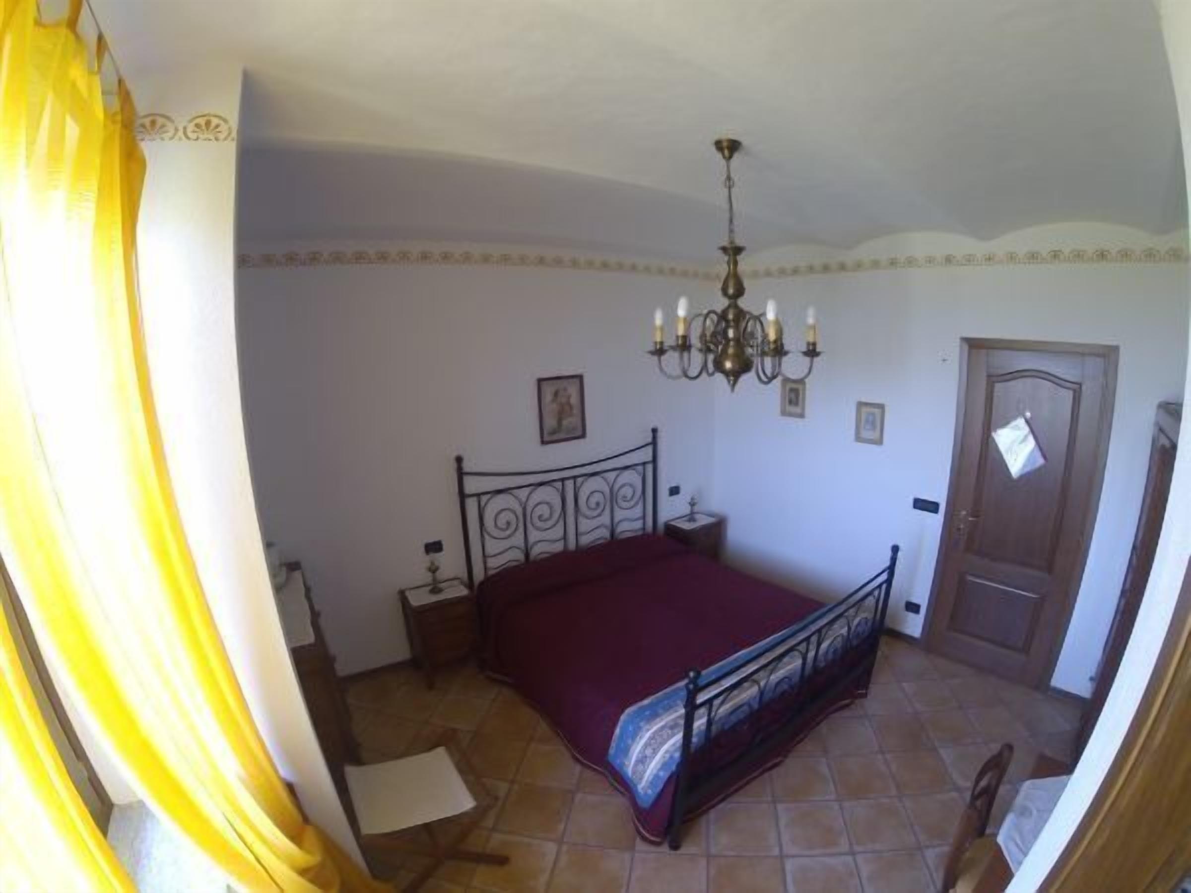 A bedroom with a bed, a chandelier, a door, and a window with curtains.