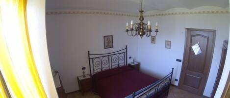 A bedroom with a bed, a chandelier, a door, and a window with curtains.