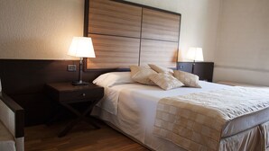 Una camera d'albergo con un letto grande, due comodini con lampade e un pannello di testata in legno, oltre a un pavimento in legno.