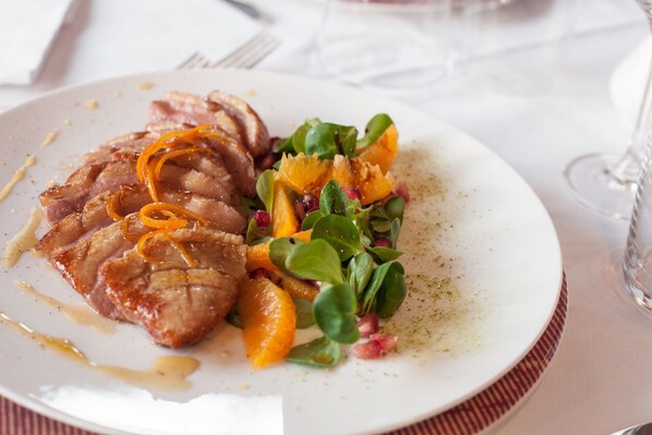 A plate with sliced meat, orange slices, and greens. - Hotel La Bettola (Carisio)