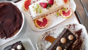 Una selezione di dolci su un vassoio, tra cui un dessert bianco con fragole e uva, un dessert al cioccolato con noci e un dessert al cioccolato fondente con biscotti.