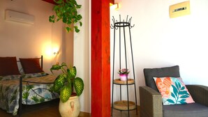 A room with a bed, a sofa, a potted plant, a wall-mounted air conditioner, and a red accent wall. - Flowery Inn Villa (Alghero)