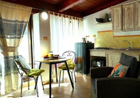 Zona pranzo con tavolo e sedie, cucina con pensili e lavello, e soggiorno con divano.