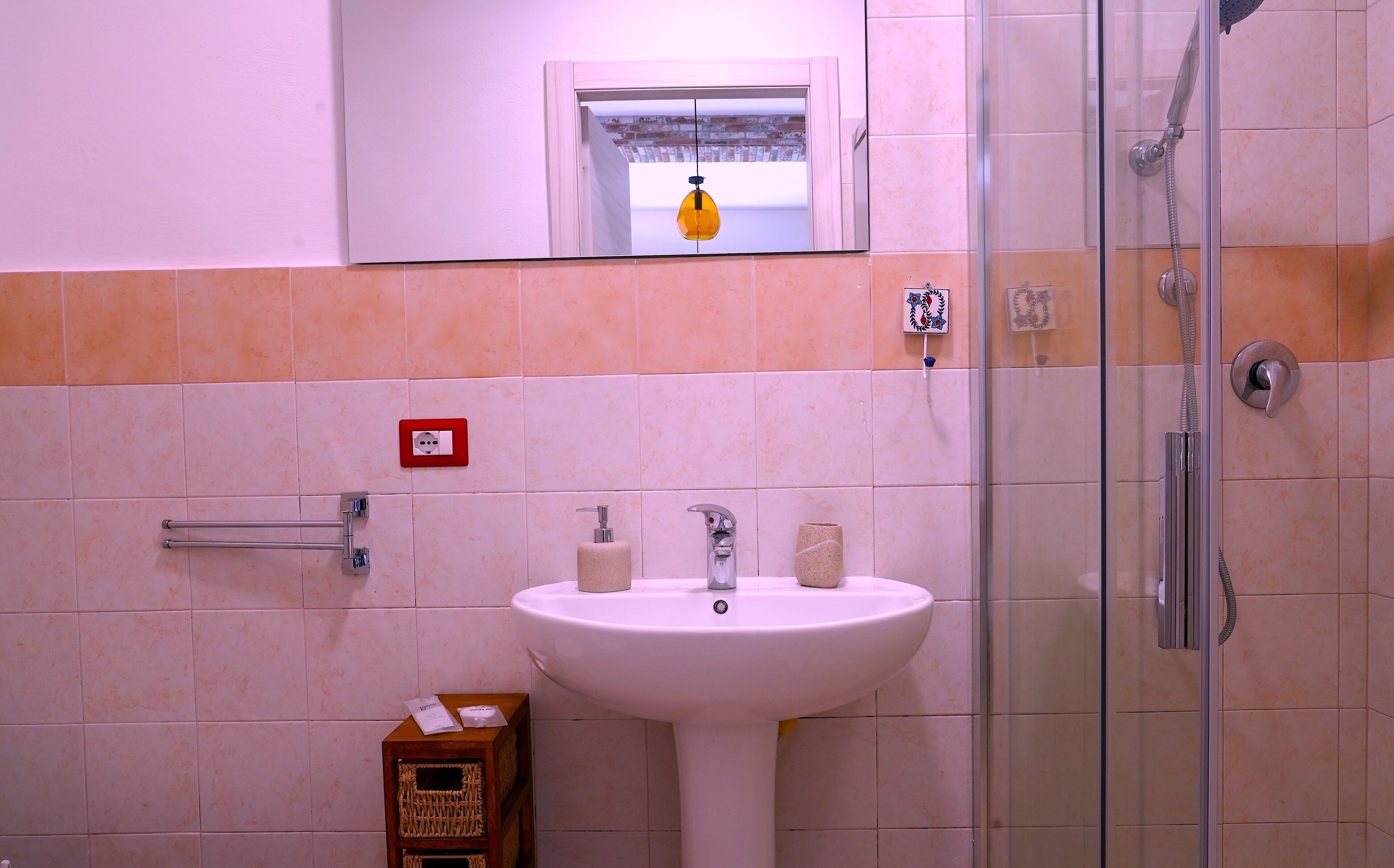 A bathroom with a white sink, a glass shower enclosure, and a small window with a hanging light.