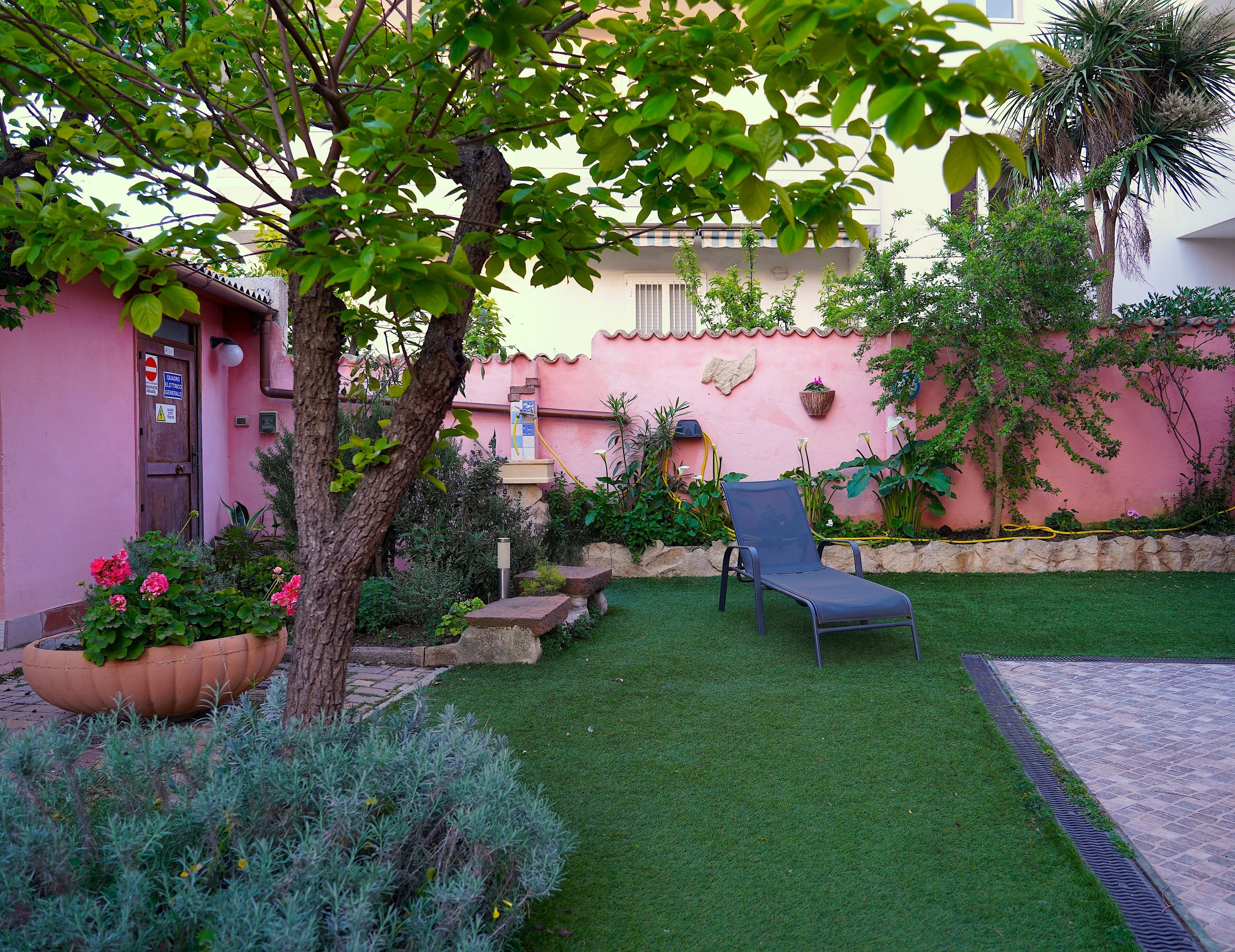 Un jardín con césped, una silla y un edificio rosa con una puerta.