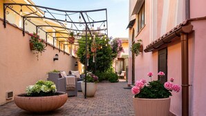 A narrow alley with a brick pathway, outdoor seating with cushions, and large flower pots. - Flowery Inn Villa (Alghero)