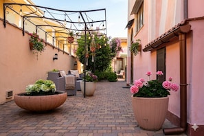 A narrow alley with a brick pathway, outdoor seating with cushions, and large flower pots.