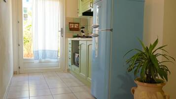 A kitchen with a blue refrigerator, green cabinets, a tiled floor, and a potted plant.
