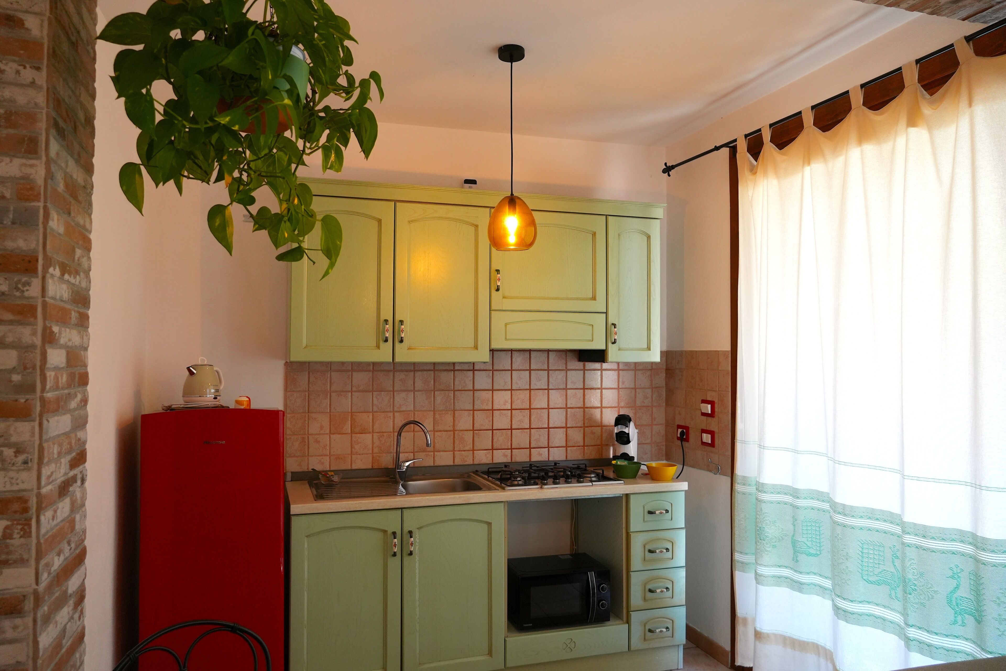 A kitchen with green cabinets, a red refrigerator, a hanging light fixture, and a microwave.
