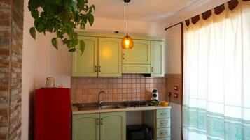 Une cuisine avec des meubles de rangement verts, un réfrigérateur rouge, un luminaire suspendu et un four à micro-ondes.