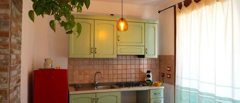 A kitchen with green cabinets, a red refrigerator, a hanging light fixture, and a microwave.