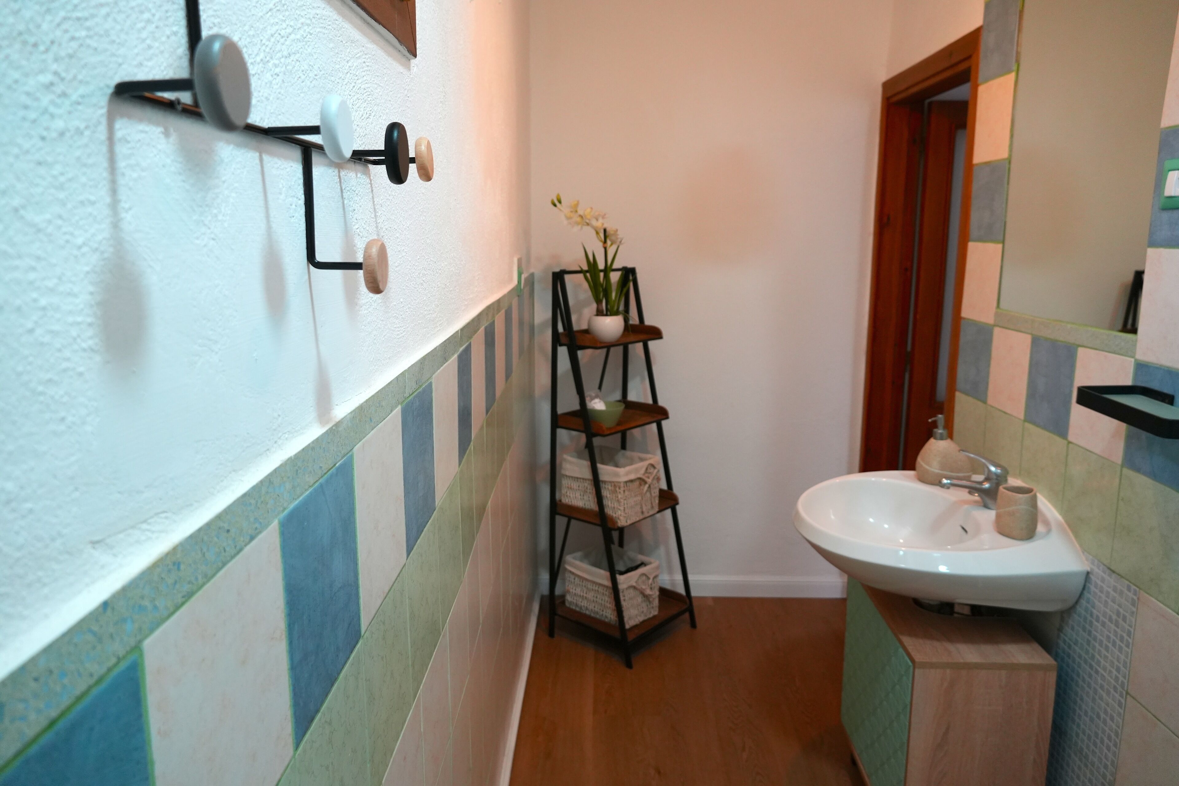 Une salle de bain avec un lavabo blanc, une étagère sur laquelle se trouve un vase et un miroir accroché au mur.