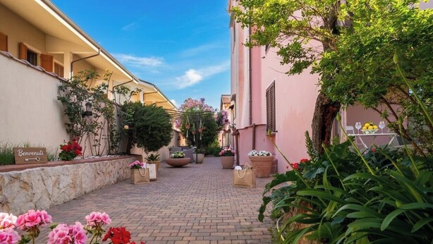 A courtyard with potted plants, a welcome sign, and a table with a fruit display. - Flowery Inn Villa (Alghero)