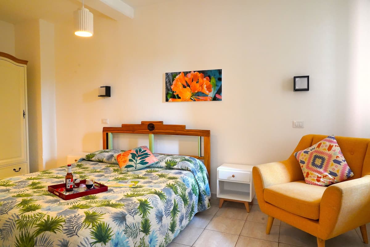 Un dormitorio con una cama, una silla, una mesita de noche y un cuadro colgado en la pared.