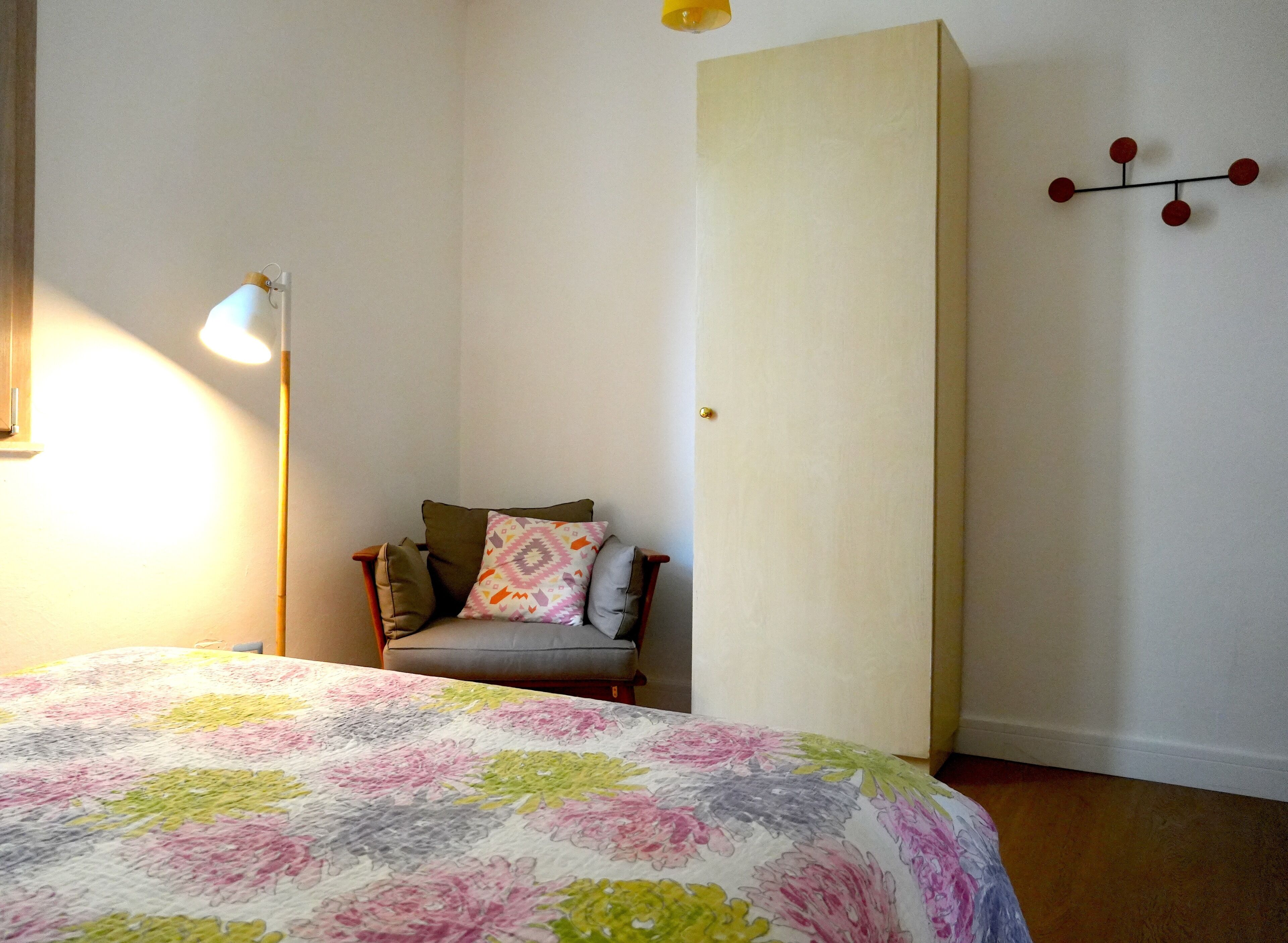 A bedroom with a bed, a chair, a lamp, and a wall-mounted light fixture.