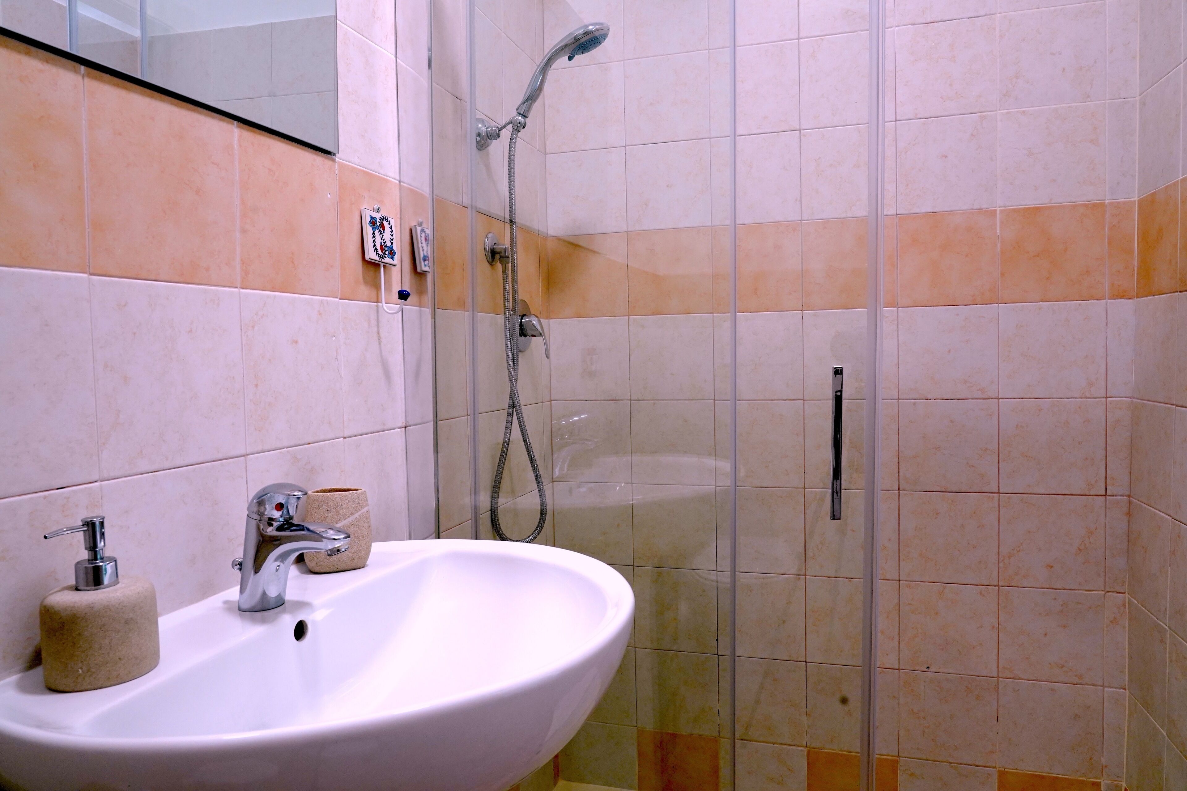 Un baño con lavamanos blanco, ducha de mano y cabina de ducha con paredes de vidrio.