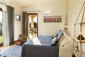 A bedroom with a bed, a painting, a lamp, and a view of the outdoors. - Tenuta Pilastru (Arzachena)